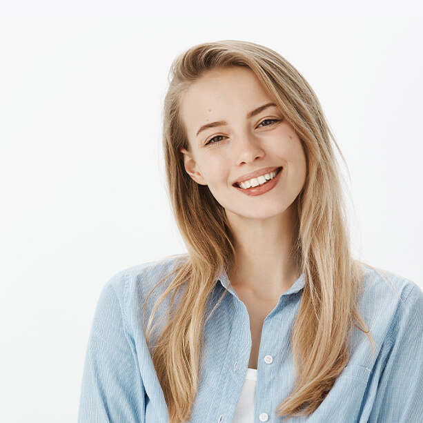 Attractive sensual woman knows how to achieve her goal. Indoor shot of positive good-looking feminine girl with bun hairstyle, smiling flirty while talking with coworker she likes over white wall.